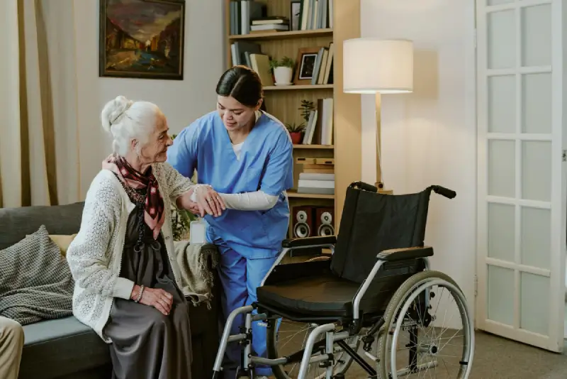 Nurse helping an older woman stand from her wheelchair in a living room