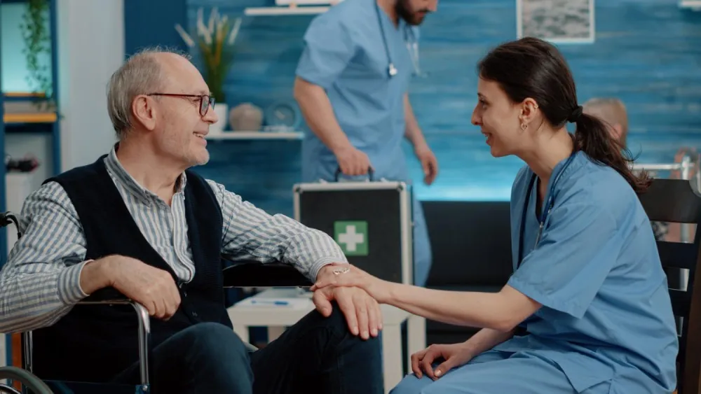 Nurse holding the hand of an older man in a wheelchair