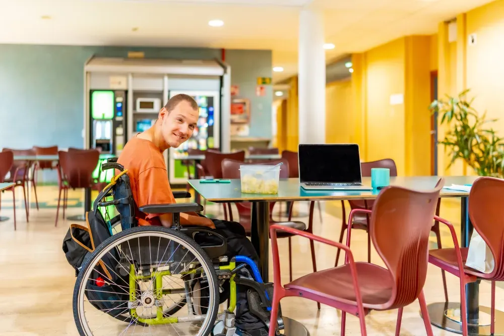 Man in a wheelchair working on a laptop at a cafe table
