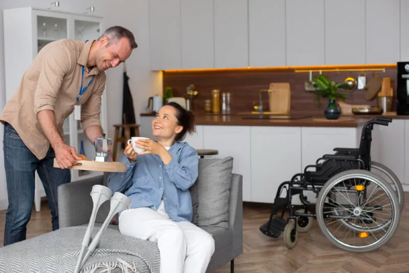 Support worker bringing a cup of tea to a woman with crutches at home