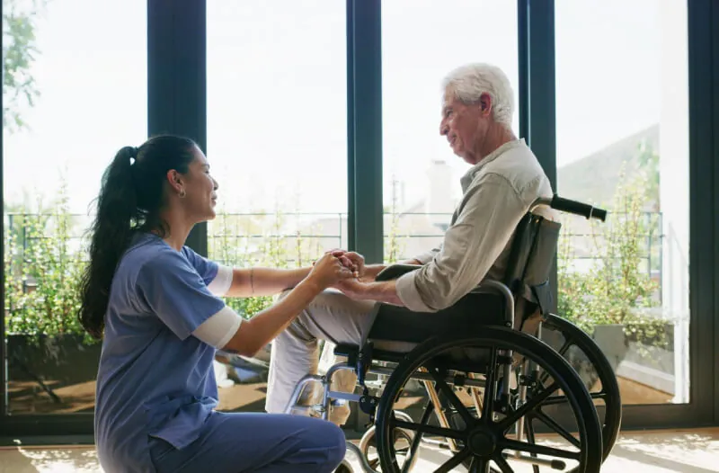 Support worker sitting with an older man in a wheelchair by a window