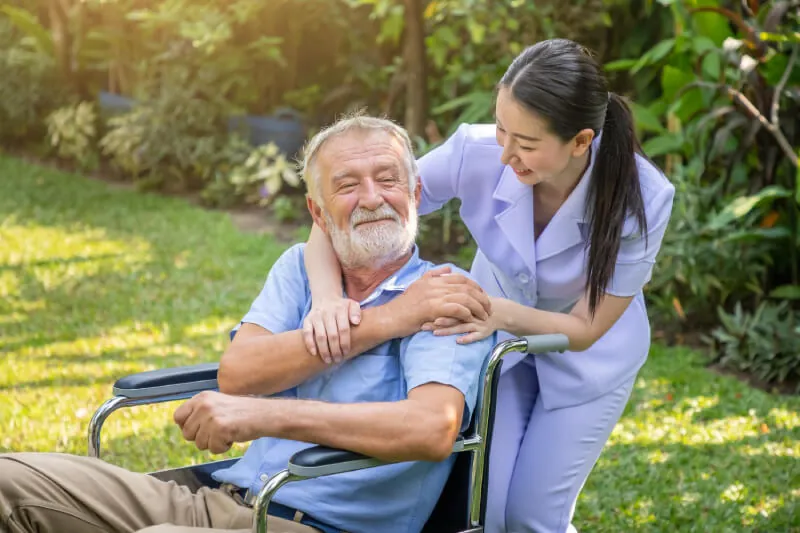 Support worker with an older man in a wheelchair in a garden