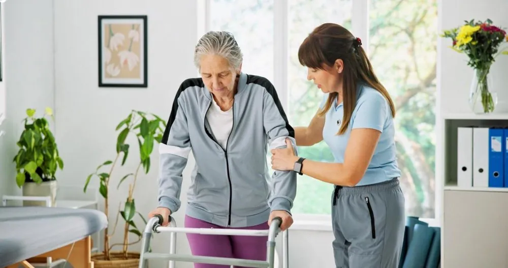 Support worker helping an older woman walk with a frame in her living room