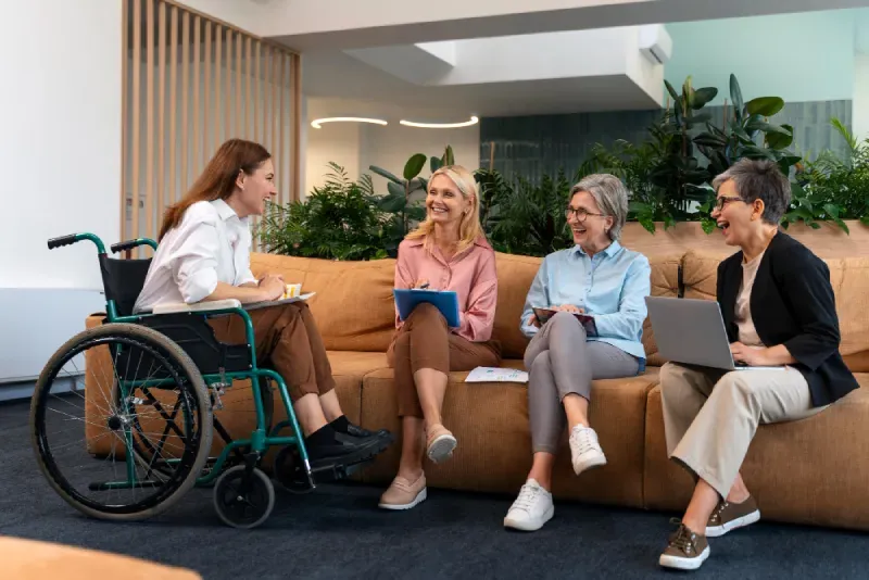 Four women, one in a wheelchair, talking together on a sofa in a shared living room