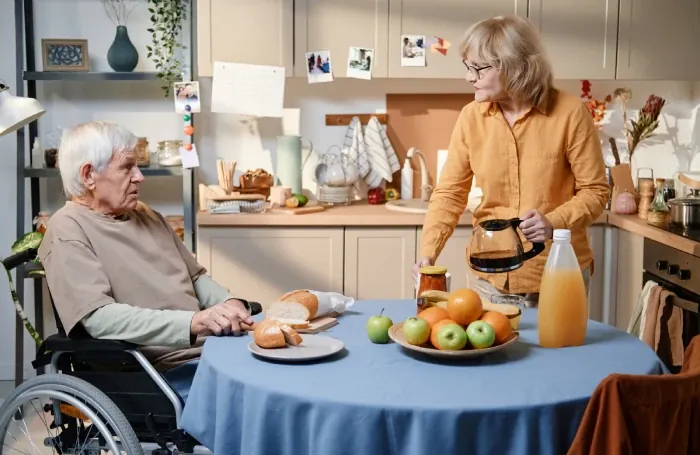 Support worker preparing breakfast for a man in a wheelchair at a kitchen table