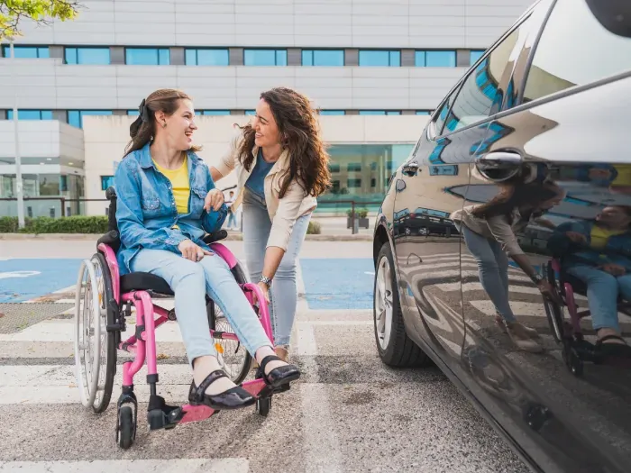 Young woman in a wheelchair talking with a support worker beside a car