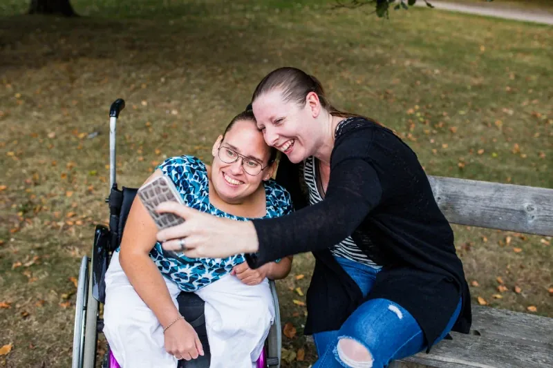 Woman in a wheelchair taking a selfie with a friend in a park
