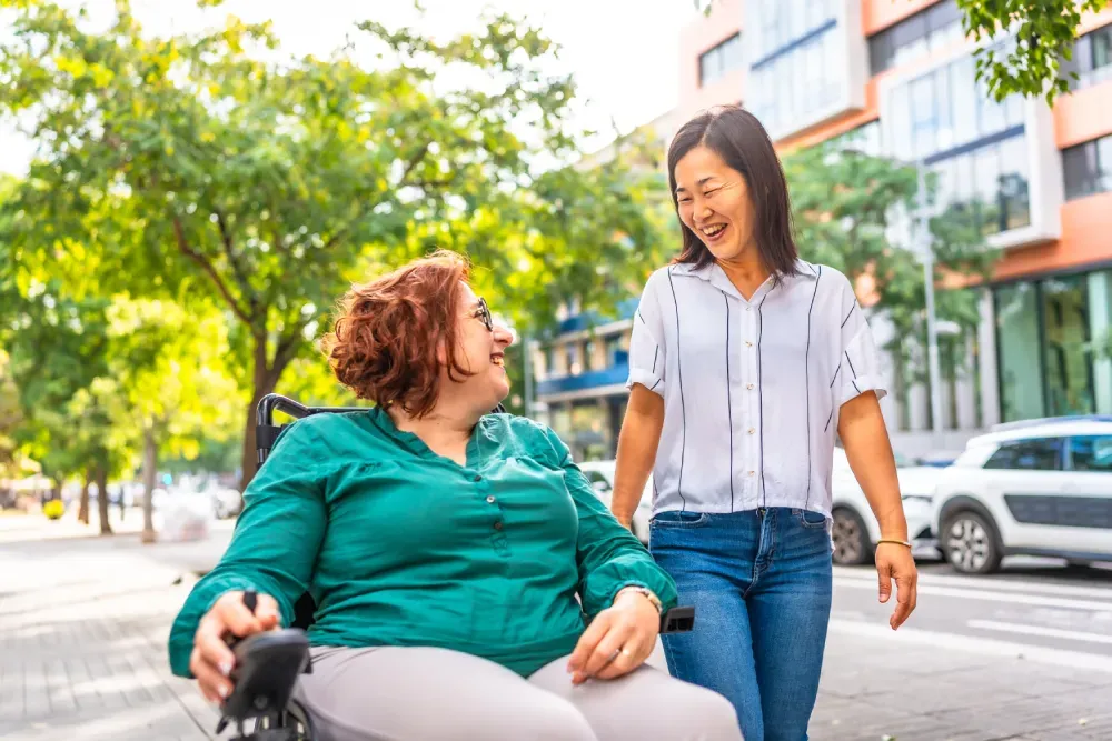 Woman in a wheelchair and a support worker chatting on a city footpath