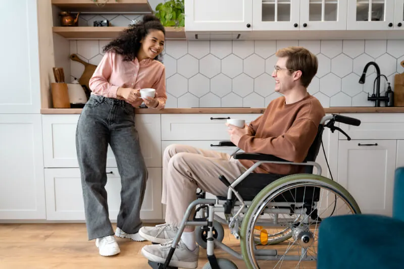 Man in a wheelchair and a support worker sharing a coffee in a kitchen