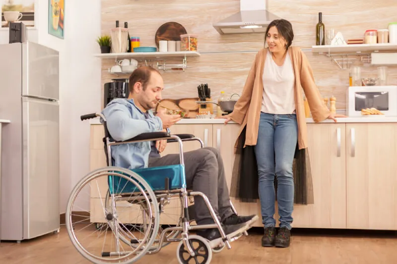 Man in a wheelchair and a support worker talking in a kitchen