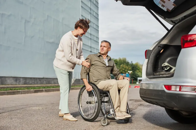 Support worker helping a man in a wheelchair beside an open car boot
