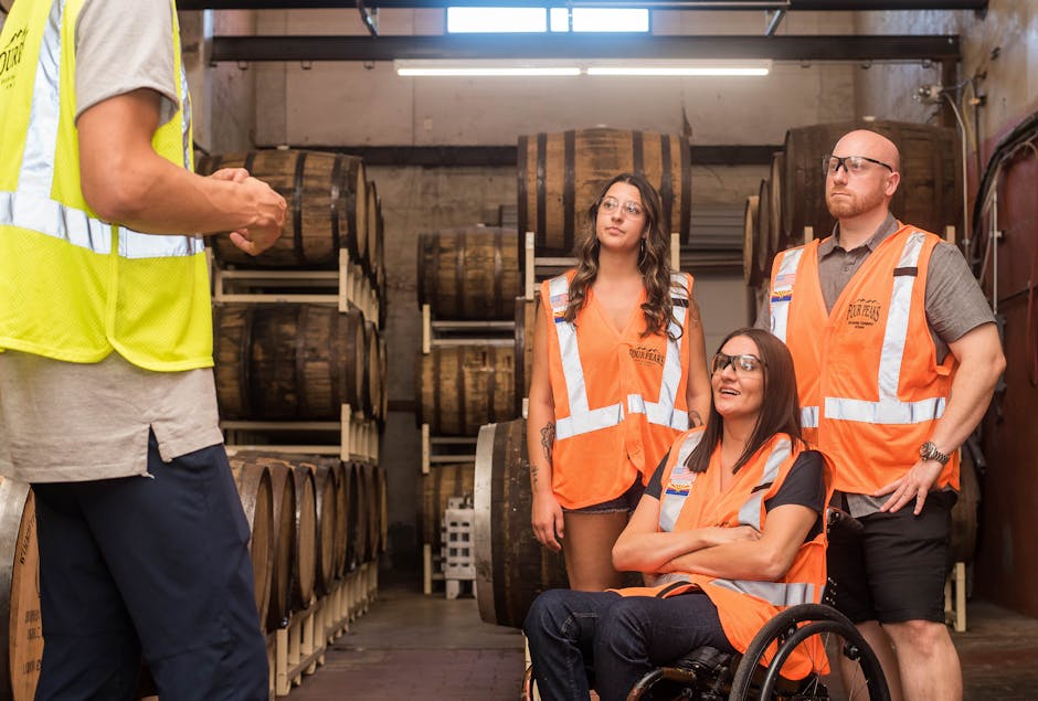 Group of adults in safety vests touring a brewery, highlighting inclusivity and accessibility.