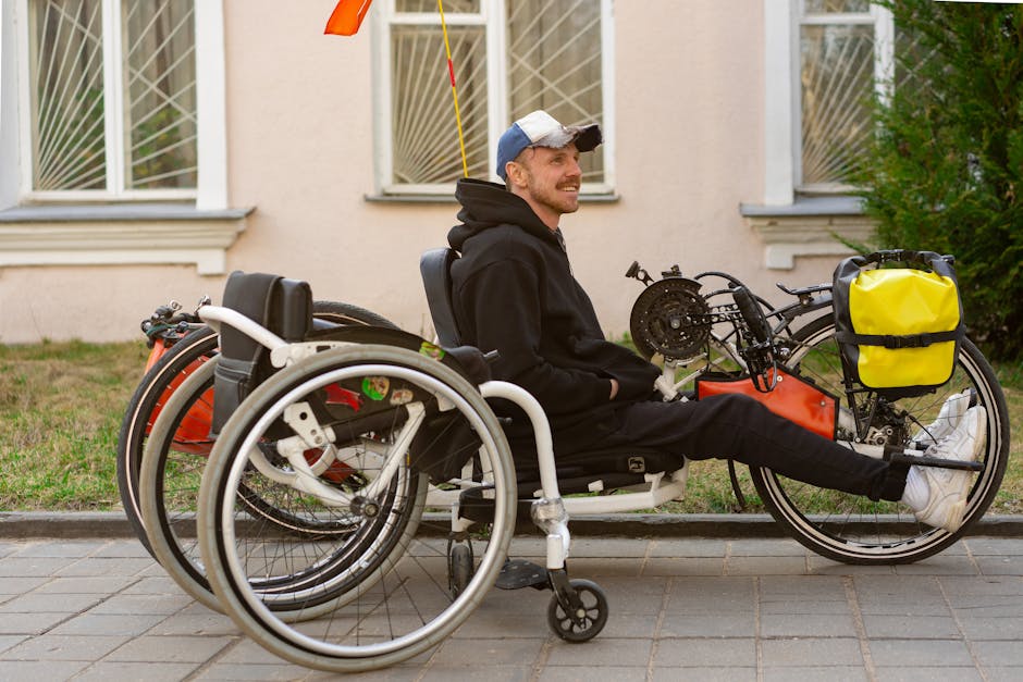 Man in a black hoodie sits smiling on a handcycle in an outdoor urban setting.